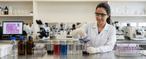 Histotecnologista no laboratório mergulhando suporte de lâminas microscópicas em frasco de coloração.